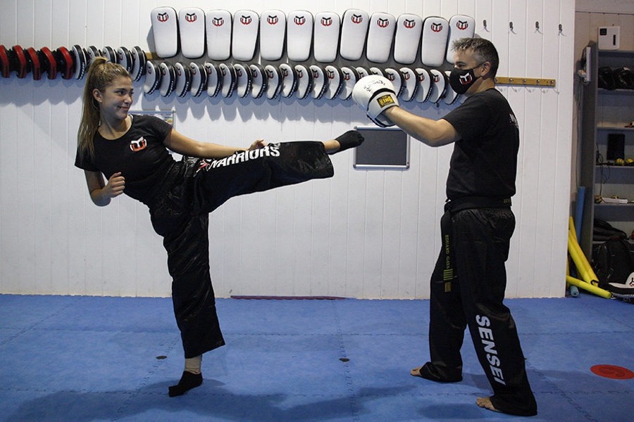 Alumna dando una patada lateral al guante del sensei en el tatami de Warriors Barcelona