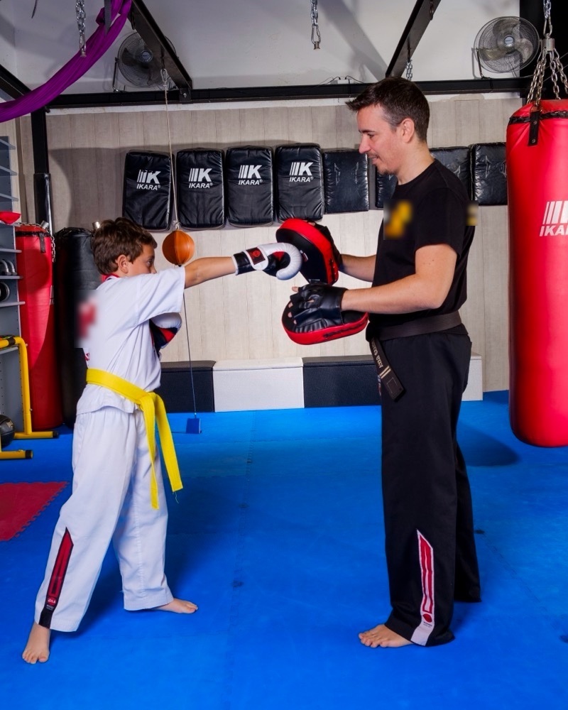 Instructor de Warriors Barcelona practicando golpeo con manoplas con un niño en el tatami