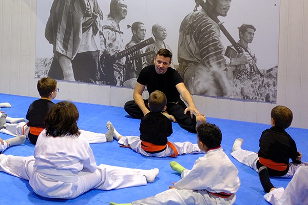 Niños con kimono estirando en el tatami junto a su instructor de karate infantil